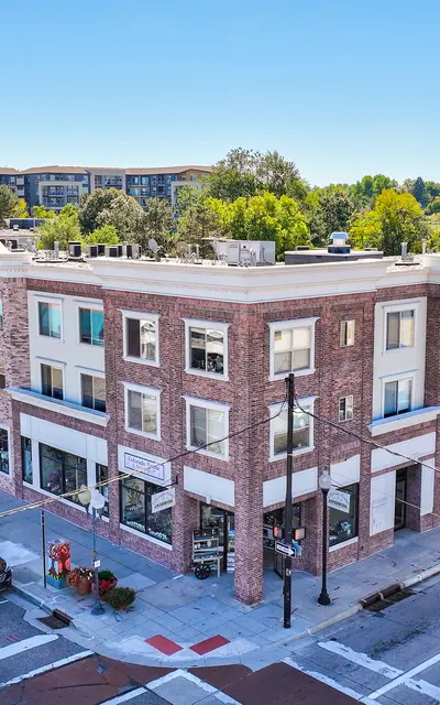 View of a multi-story brick building at a street intersection, featuring shops on the ground floor and residential units above.