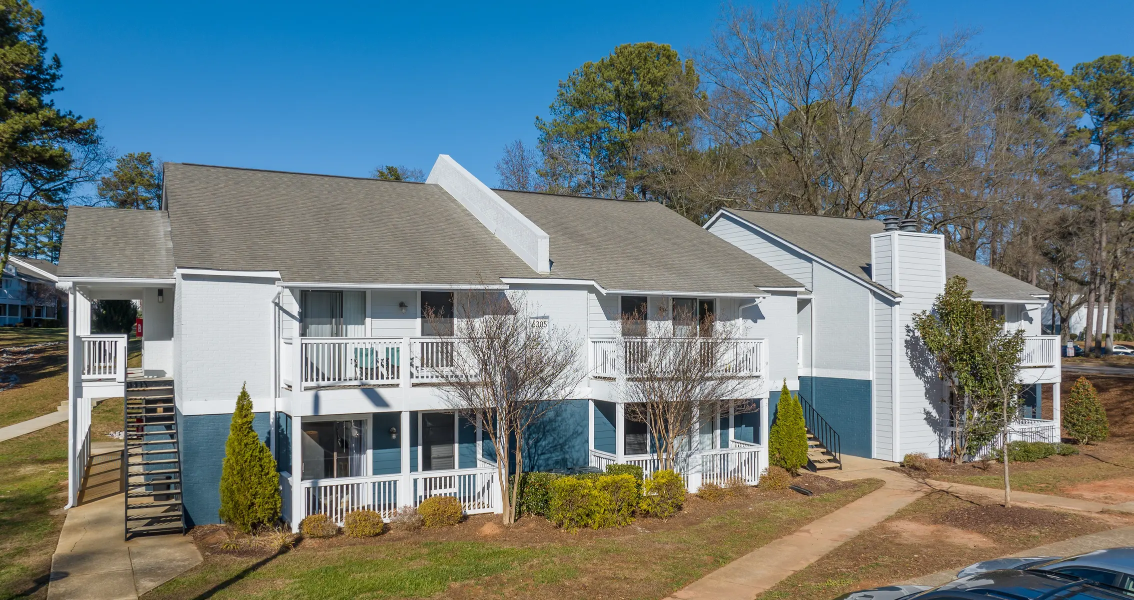 Aerial view of a multi-unit apartment complex featuring two buildings with balconies, green landscaping and a clear blue sky.