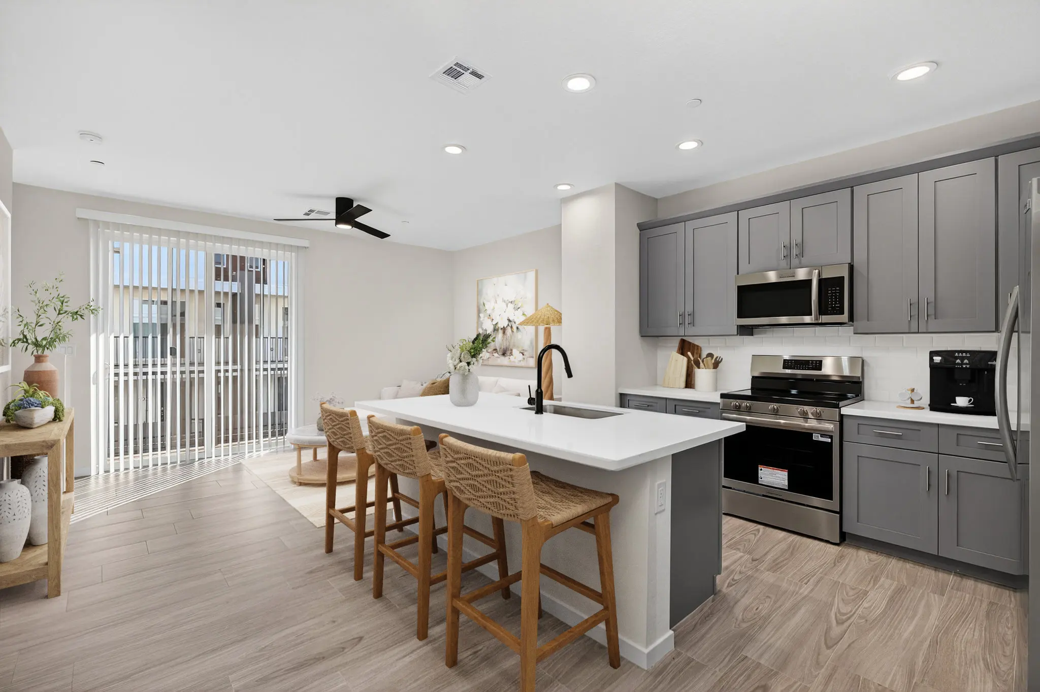 A modern kitchen featuring gray cabinetry, stainless steel appliances, and a large island with bar stools. There are large windows allowing natural light, and a cozy aesthetic with decorative plants.