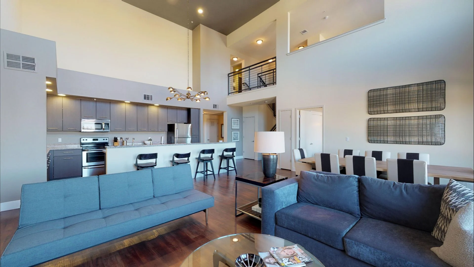 Contemporary Living Room with Open Kitchen A modern living room area featuring a blue sofa, a coffee table, and a dining area with stylish seating. The kitchen is open and includes modern appliances and a bar counter with stools.