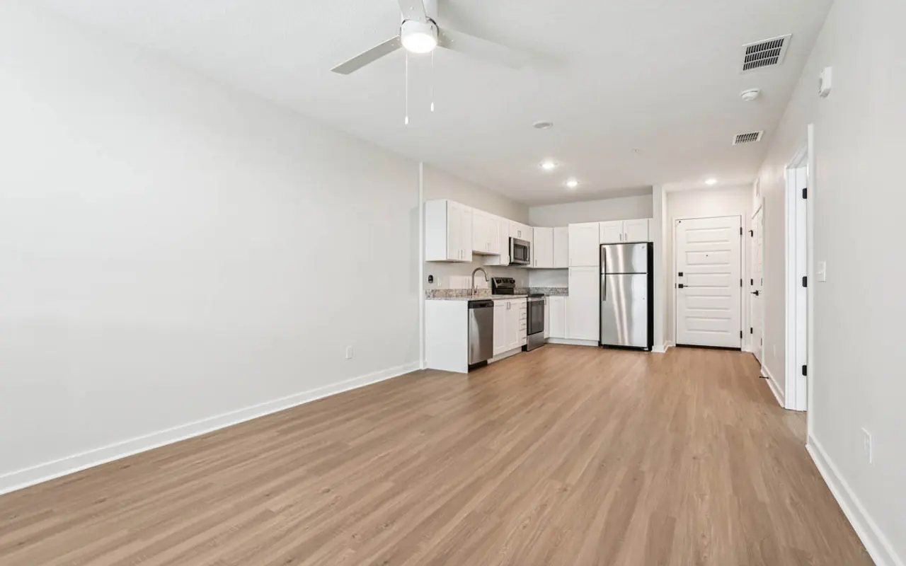 Modern Apartment Interior Interior of a modern apartment with wooden flooring, featuring a kitchen area with stainless steel appliances and a living space devoid of furniture.