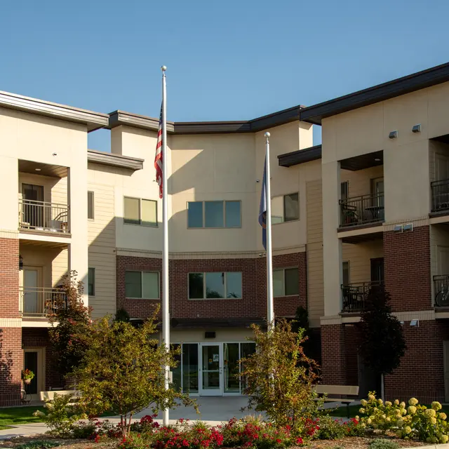 Modern apartment building with flagpoles and landscaped entrance.