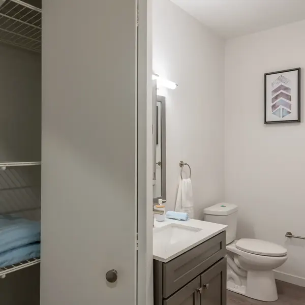 Contemporary bathroom featuring a gray vanity, mirror, and minimal decor. Shadowed wall with open shelving next to a blue towel.