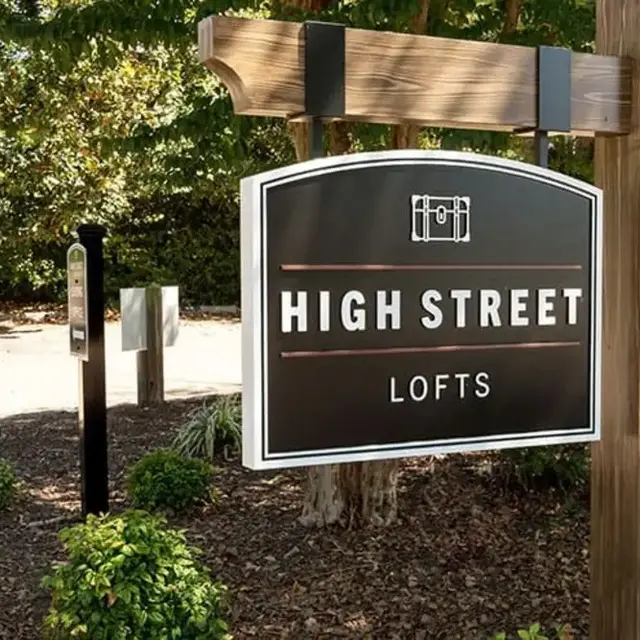 A sign for High Street Lofts, made of wood with white text on a black background, surrounded by greenery.