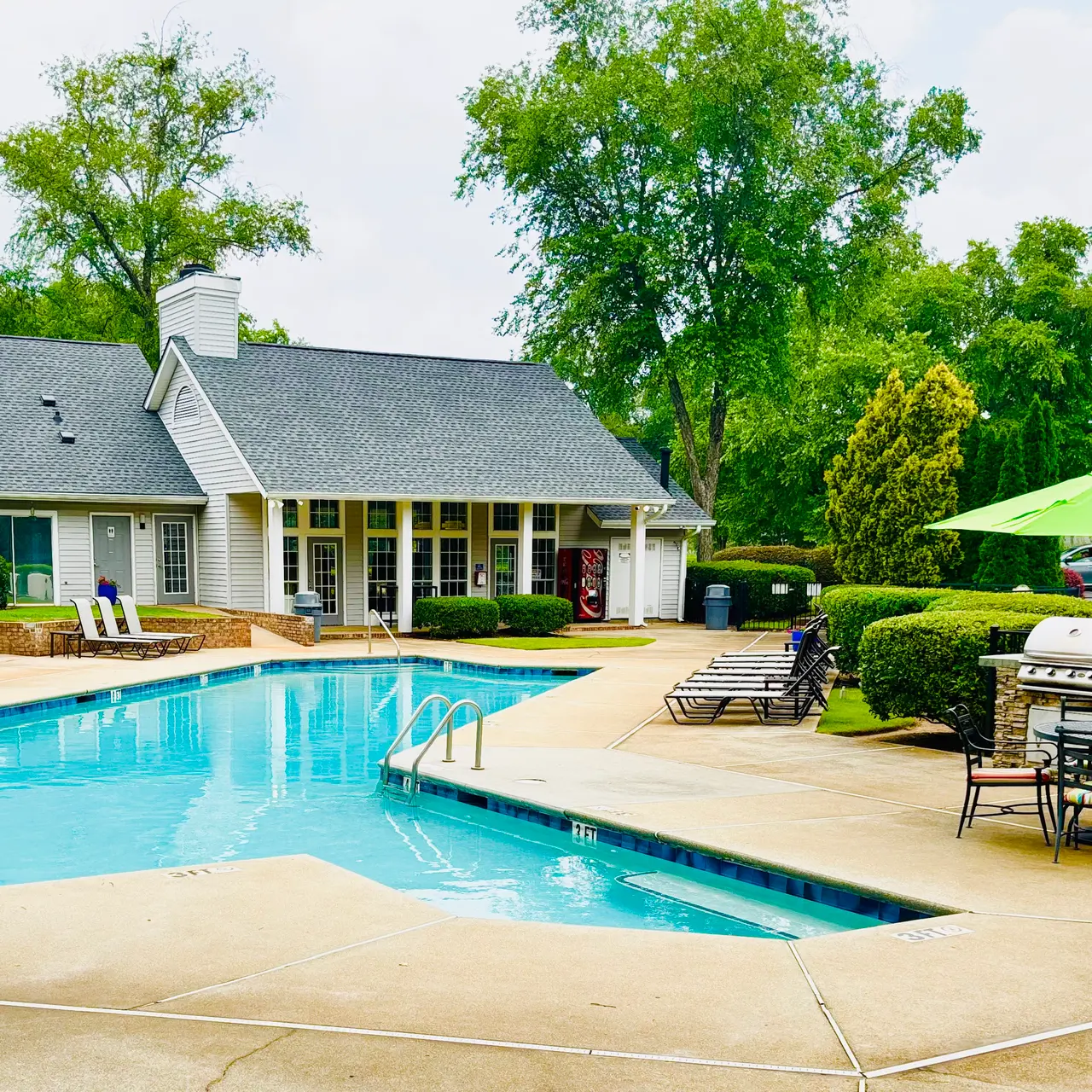 A serene pool area at an apartment complex with lounge chairs and a clubhouse in view.