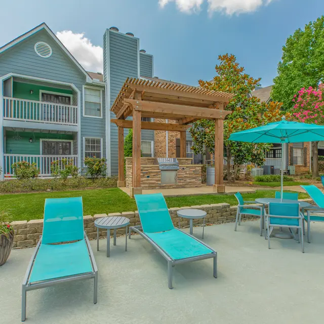 A brightly colored outdoor pool area featuring turquoise lounge chairs and tables, with a pergola in the background, surrounded by greenery and flowers.