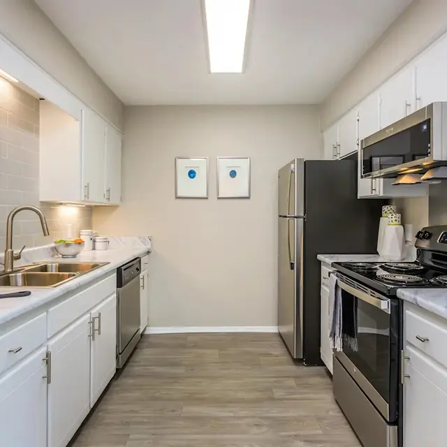 Modern kitchen with stainless steel appliances, white cabinets, a marble countertop, and light-colored flooring.