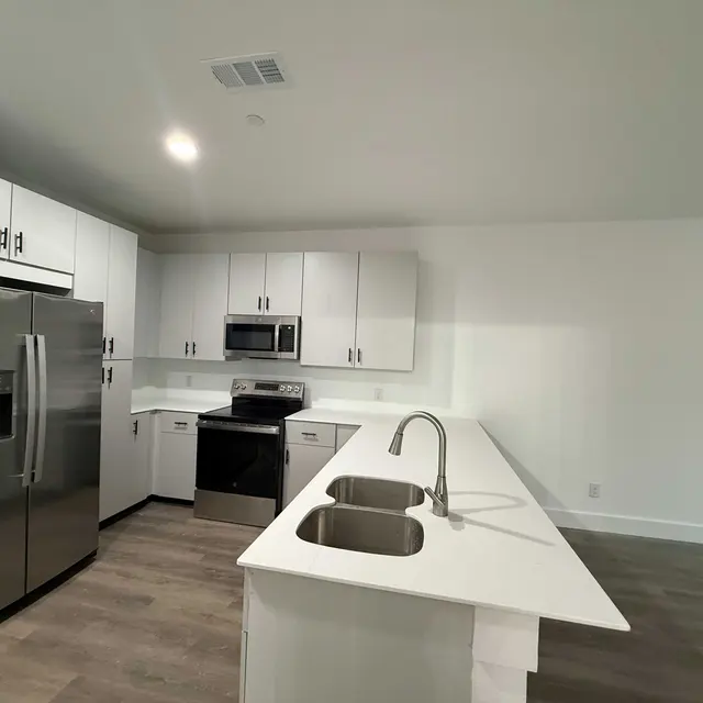 A modern kitchen featuring stainless steel appliances, including a refrigerator and an oven, white cabinets, and a spacious island with a double sink.