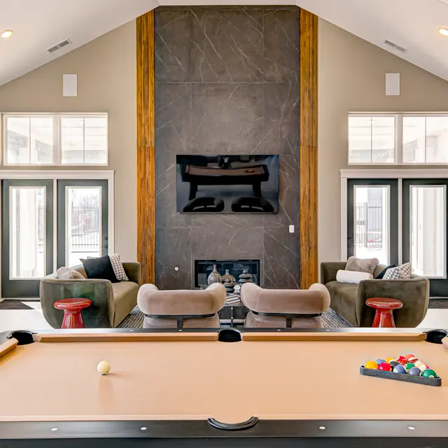Contemporary game room featuring a pool table, cozy seating area, large windows, and a stone accent wall with a TV above a fireplace.