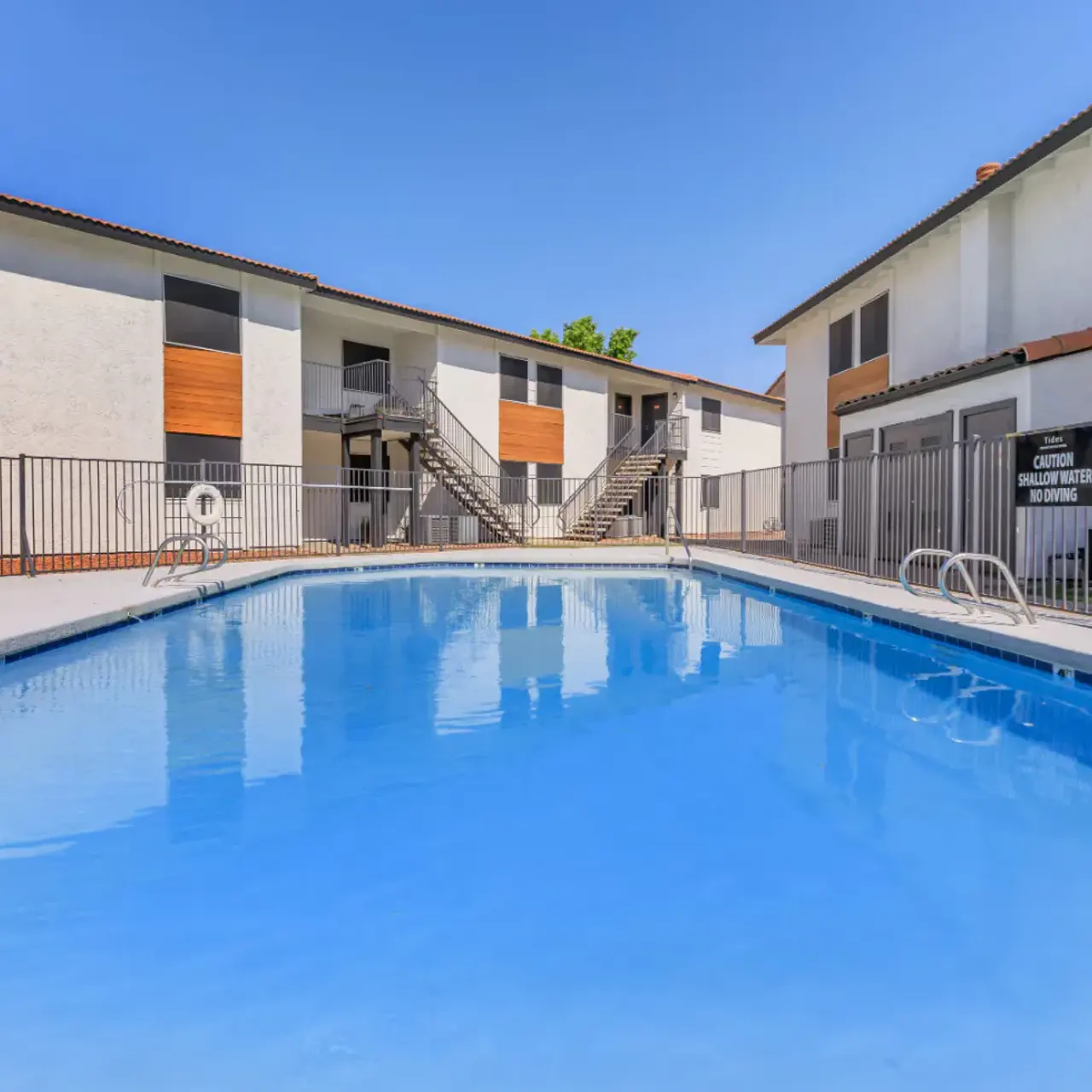 A clear swimming pool surrounded by residential buildings with a fence.