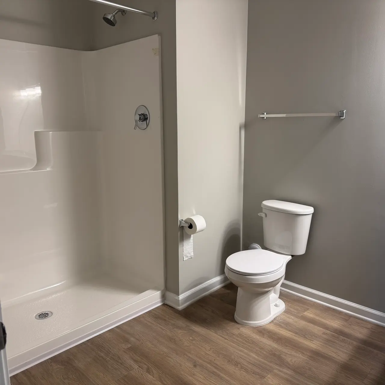 A modern bathroom featuring a white shower stall, a white toilet, and a dark blue vanity with a granite countertop, set against a light gray wall.