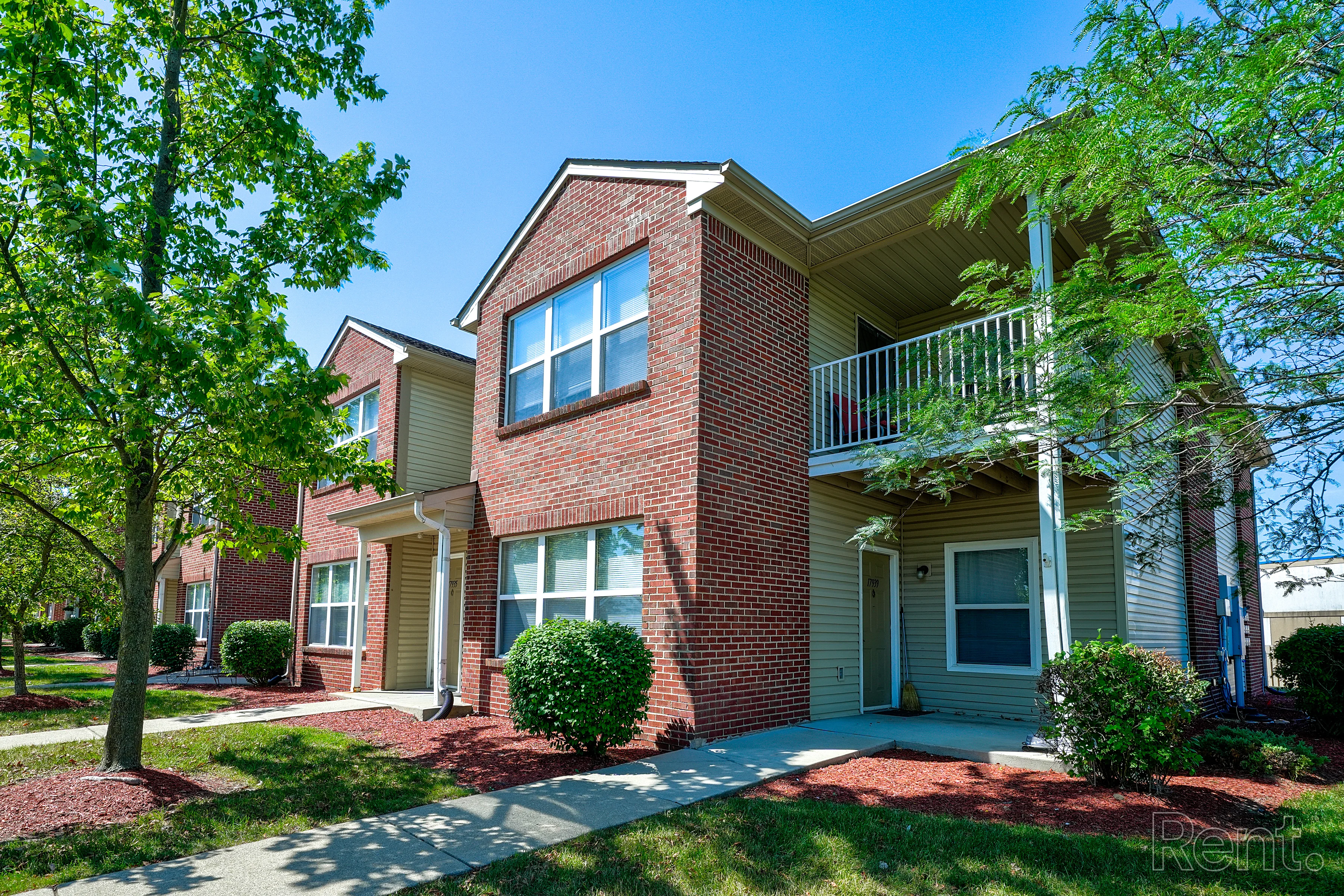 Two-Story Apartment Building Exterior view of a two-story apartment building with brick facade and balcony, surrounded by greenery.