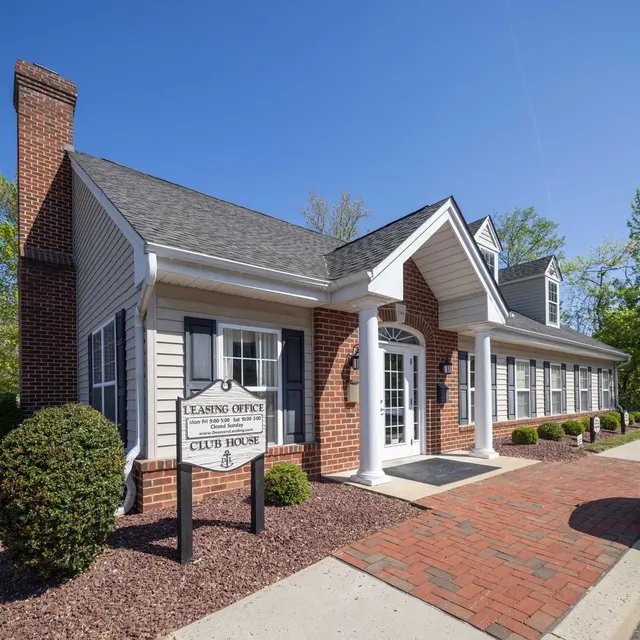 An exterior view of a leasing office and club house with a brick facade, white columns, and a landscaped entrance.