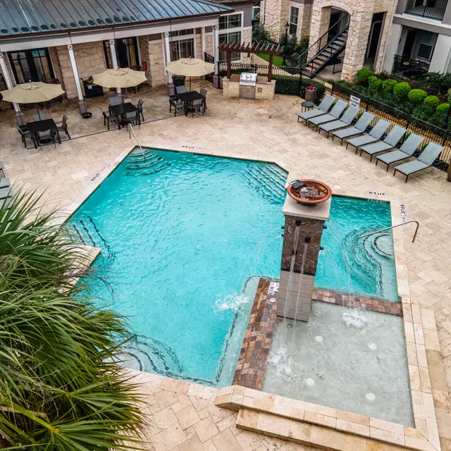Aerial view of a swimming pool area with a hot tub, lounge chairs, and umbrellas.