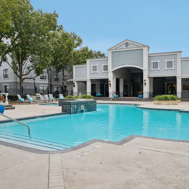 Swimming pool area at an apartment complex featuring lounge chairs and a modern building in the background.