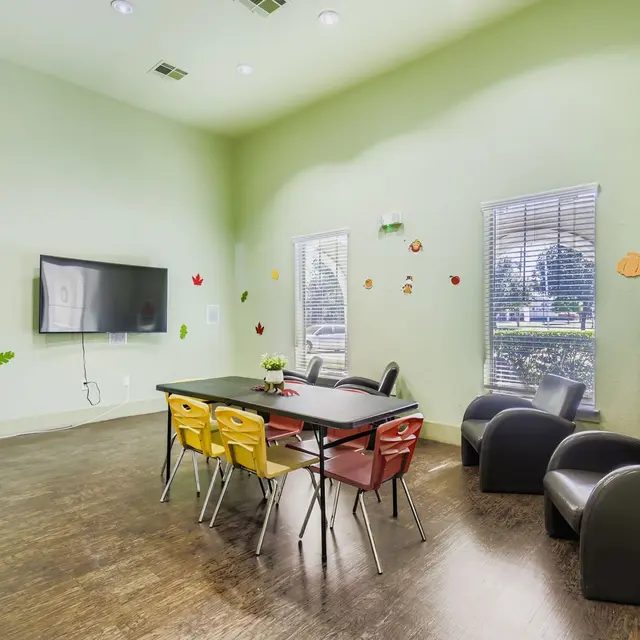 Brightly colored chairs around a table in a spacious room with green walls and a television.
