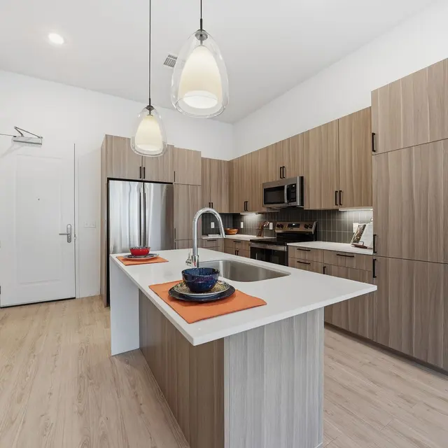 Modern kitchen with wooden cabinets, stainless steel appliances, an island with a sink, and pendant lighting.