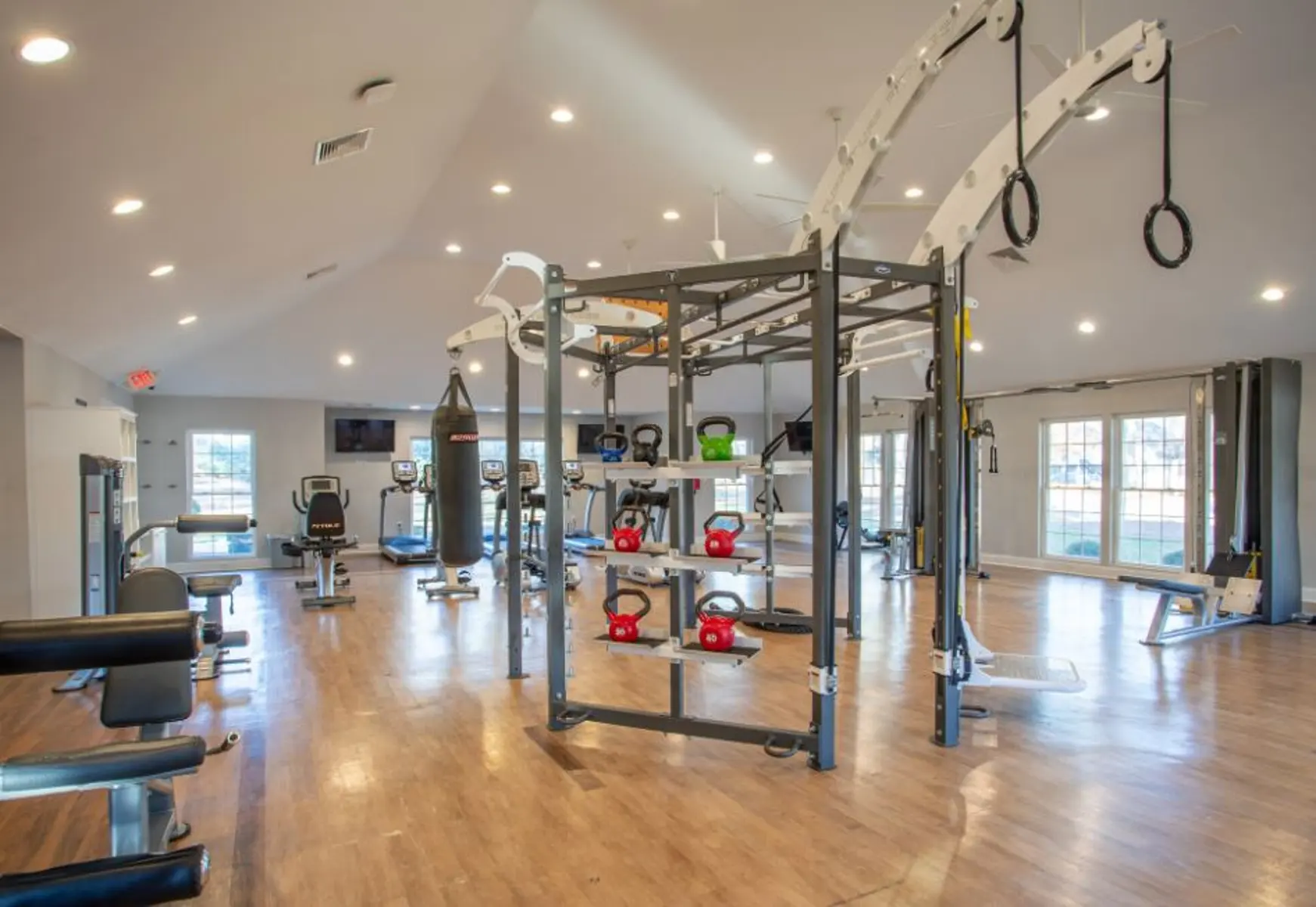 A spacious gym interior featuring various workout equipment including weight machines, kettlebells, a punching bag, and a multi-use exercise station.