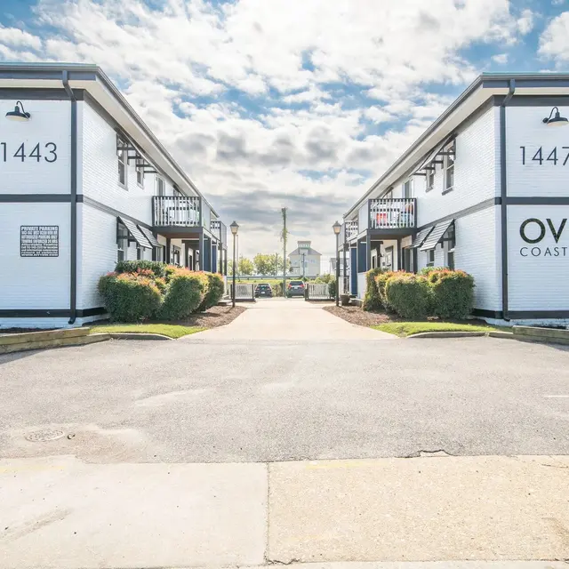 Exterior view of two buildings numbered 1443 and 1447 with a paved pathway in between, under a partly cloudy sky.