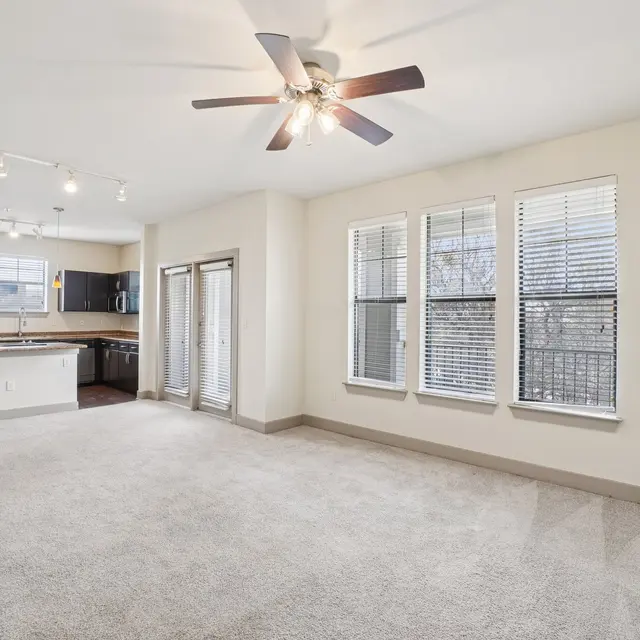 Spacious modern apartment living room with carpet, large windows, and open kitchen area.