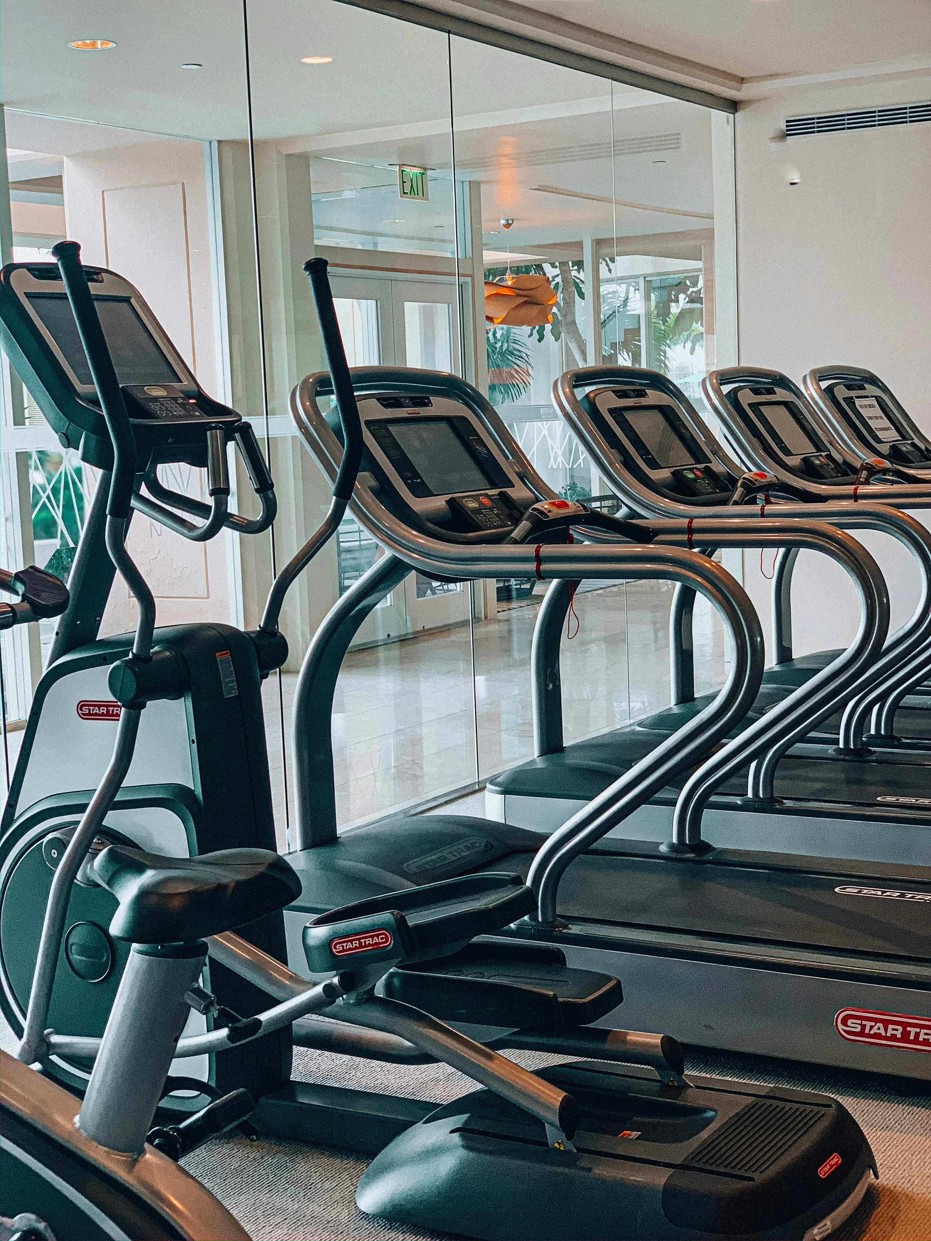 Rows of elliptical machines in a fitness center, with large windows reflecting the outdoor view and a modern interior design.
