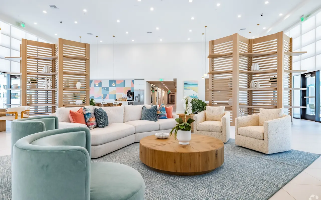 A modern lounge area featuring a large sectional sofa, light color scheme, round wooden coffee table, and decorative chairs, surrounded by wooden decorative partitions and bright lighting.