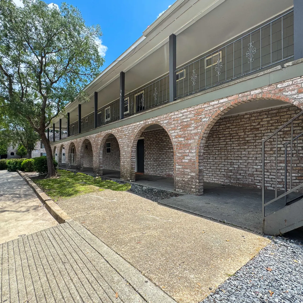 Exterior view of a multi-story apartment complex featuring arches, a staircase, and a tree.
