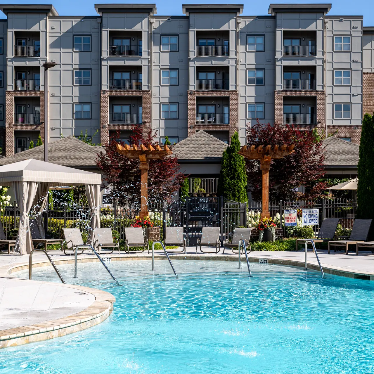 Modern Apartment Complex Pool Area A view of a modern apartment complex's swimming pool area, featuring lounge chairs, a cabana, and landscaping with trees