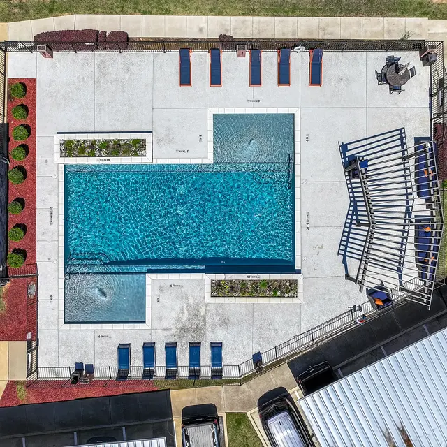 Aerial view of a swimming pool area with lounge chairs, landscaping, and a shaded seating area.