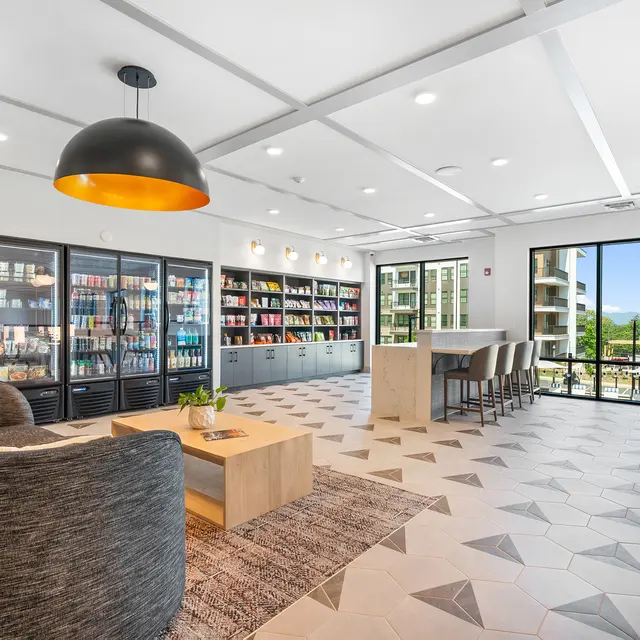 A modern lounge area with a large bookshelf and seating arrangements, featuring a cozy coffee table and large windows showing a scenic view.