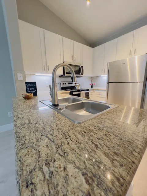 A modern kitchen featuring granite countertops, stainless steel appliances, and wooden cabinets. A sink with a faucet is in the foreground, while the backdrop shows more cabinets and a stove.