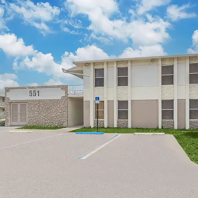 Exterior view of a two-story apartment building with a stone facade and a clear blue sky in the background.