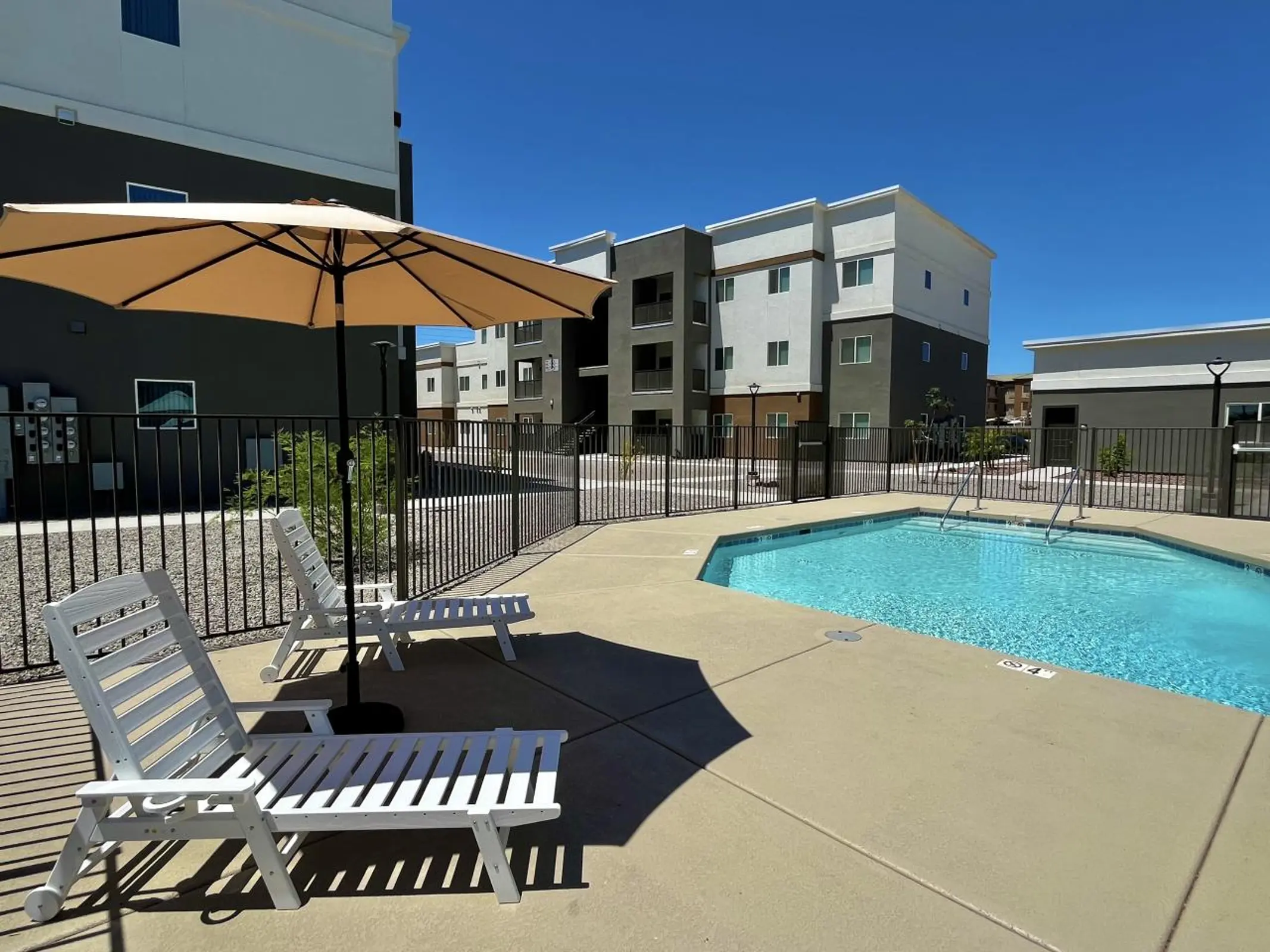 Swimming pool beside lounge chairs, an umbrella and a black metal fence.