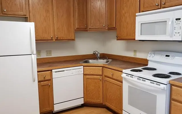 Kitchen at Twin Cedars Apartments in Helena, Montana, featuring oak cabinets, white appliances, and red countertops with ample workspace