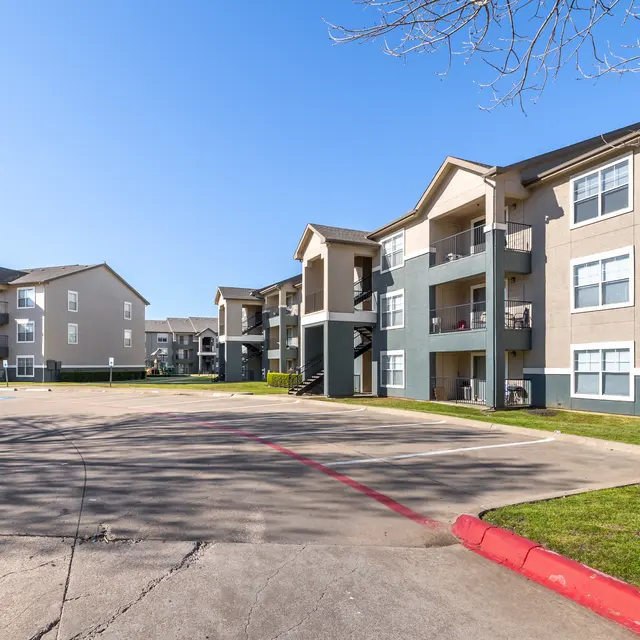 A view of a landscaped apartment complex with multiple buildings and a paved parking area.