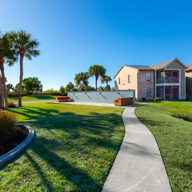 A landscaped path winding through a green lawn with palm trees and a view of a residential building in the background.