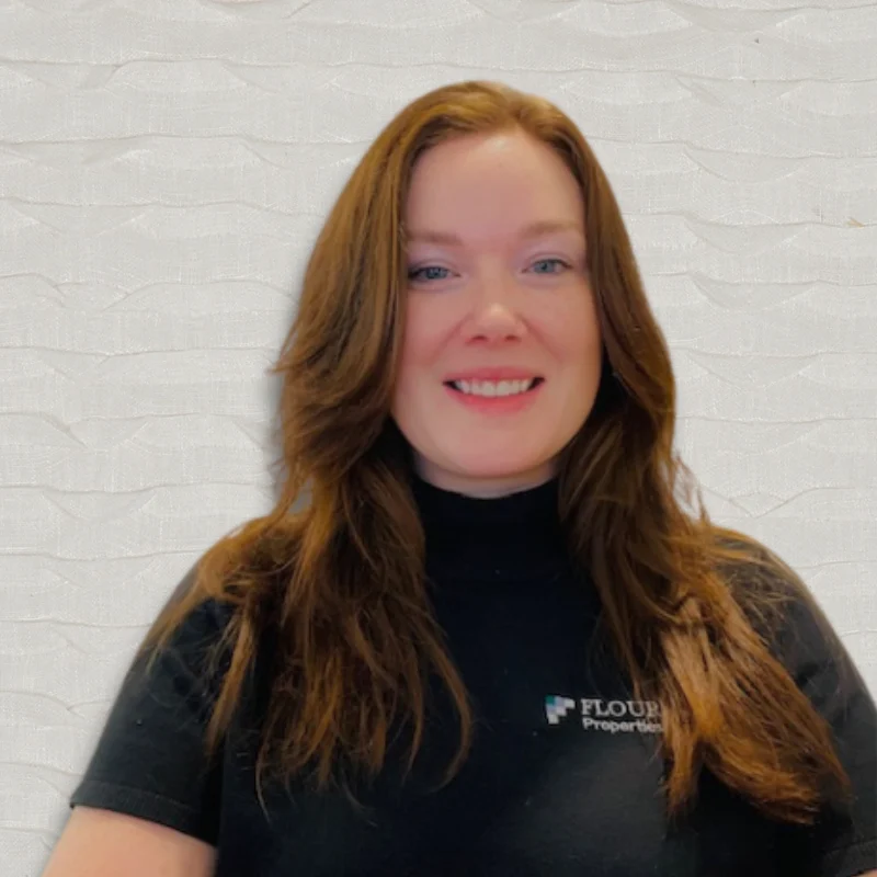 A woman with long brown hair and a black shirt, smiling against a light textured background.