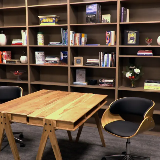 A modern office space featuring a wooden table and two stylish chairs in front of a large bookshelf filled with books and decorative items.