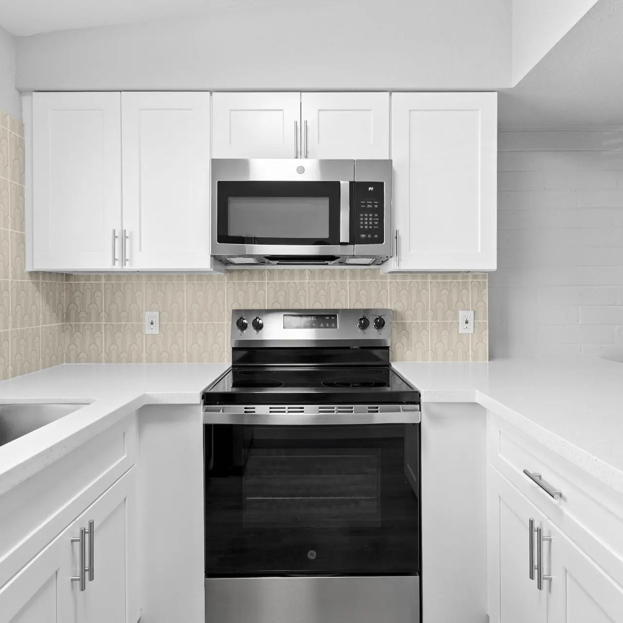 Modern Kitchen Interior A modern kitchen featuring white cabinetry, a stainless steel stove, a microwave above it, and a stainless steel sink. The countertops are white, and the walls have a light-colored tiled backsplash.