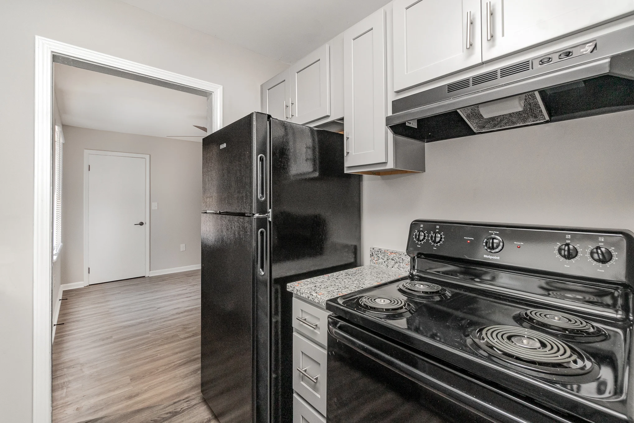 Modern kitchen featuring a black refrigerator, black stove, and light gray cabinetry with granite countertops. Spacious design.