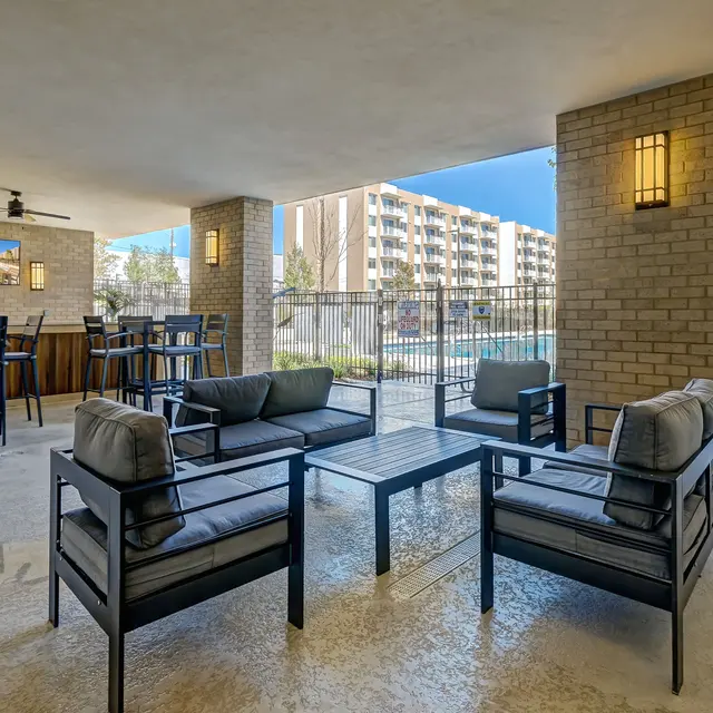 A modern outdoor lounge area with comfortable seating, a coffee table, and a view of a pool and apartment building in the background.