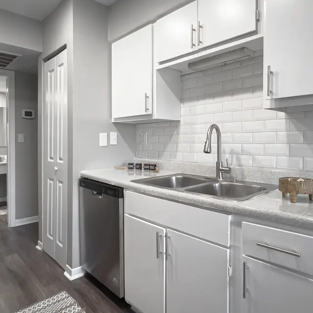 Modern kitchen with grey cabinets, stainless steel sink, and dishwasher; features a white subway tile backsplash and wooden accents.