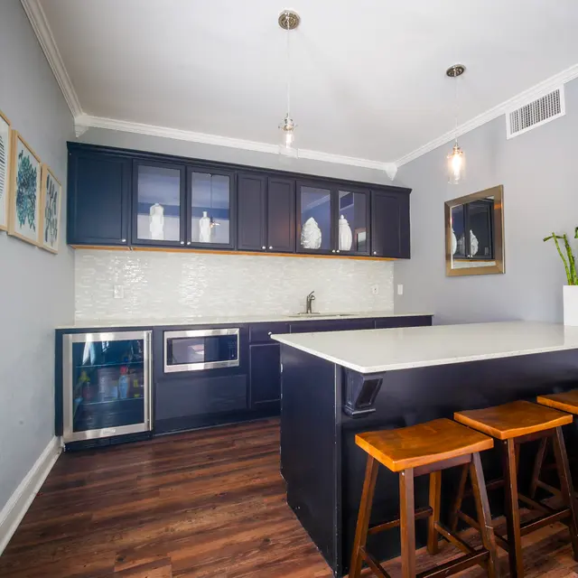 A modern kitchen featuring dark wooden cabinetry, a white countertop, and a small dining area with wooden stools.