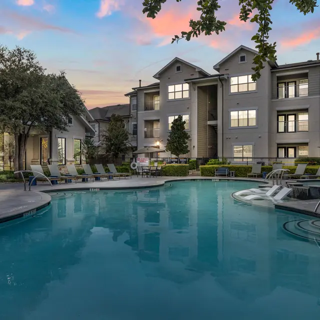 A serene swimming pool area in an apartment complex during the evening with a beautiful sky.