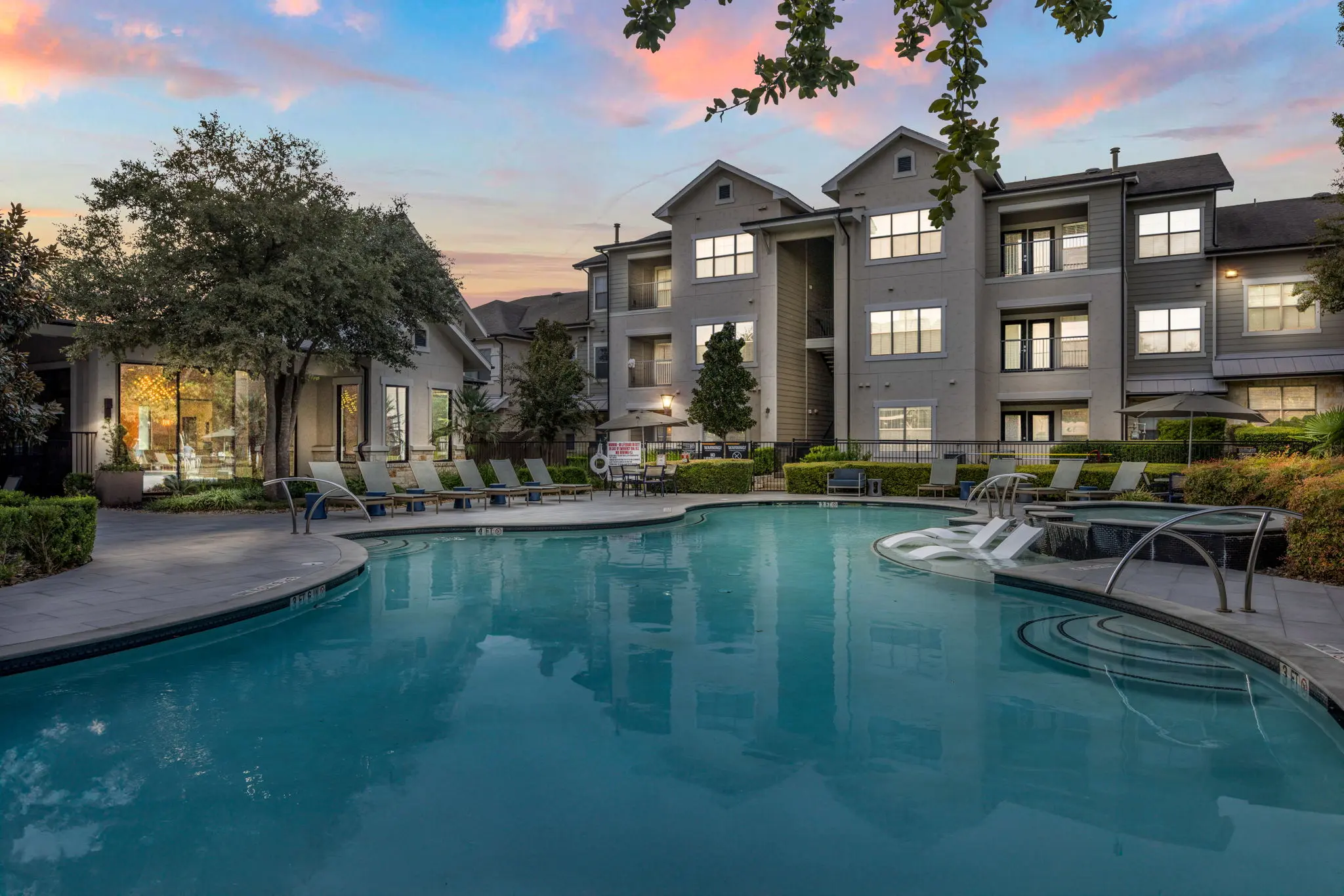 A serene swimming pool area in an apartment complex during the evening with a beautiful sky.