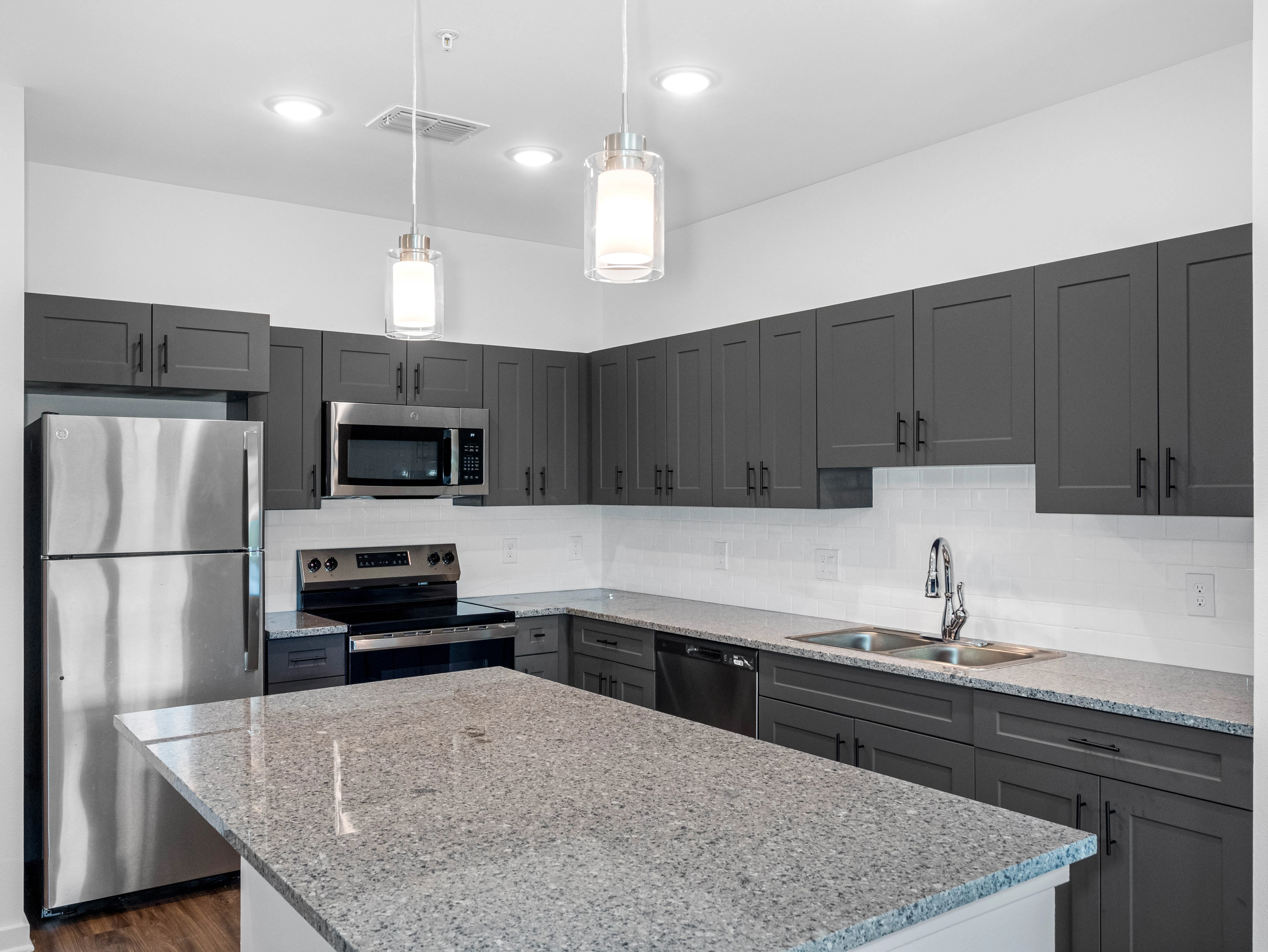 A modern kitchen featuring dark cabinets, stainless steel appliances, and a large granite island.