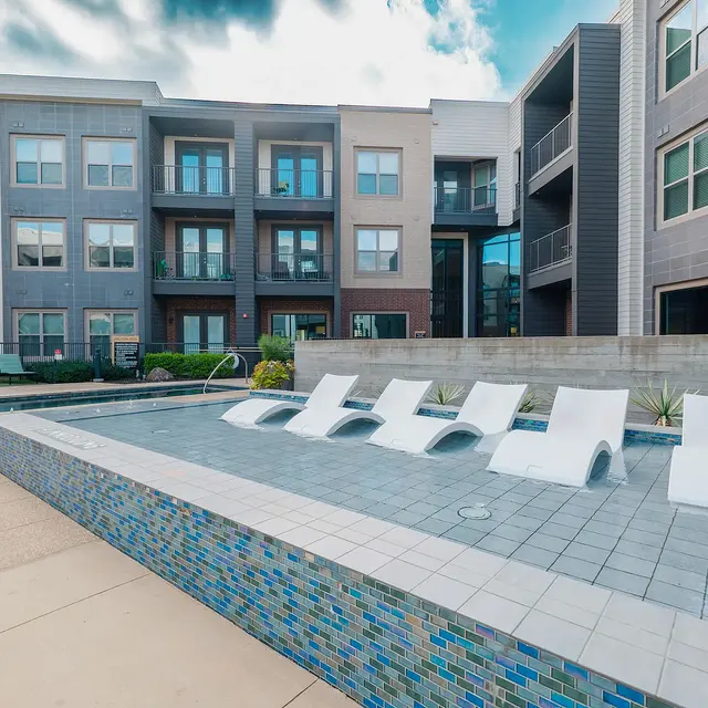 A modern pool area with lounge chairs in a residential complex, surrounded by contemporary apartment buildings.