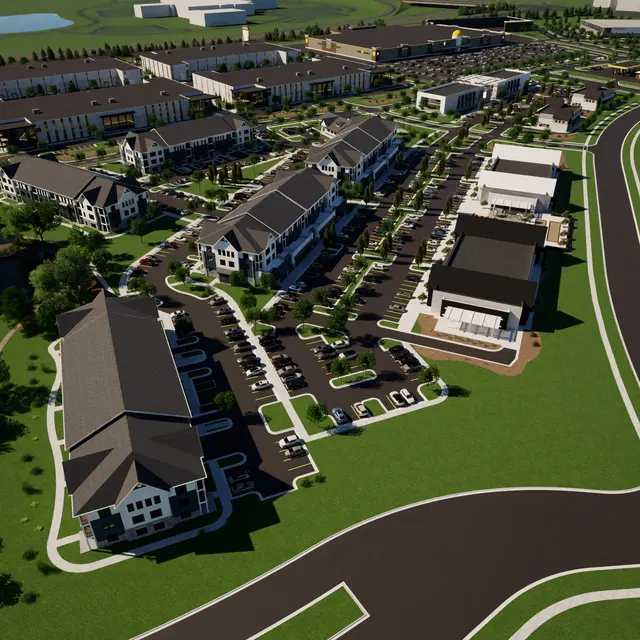 Aerial view of a modern mixed-use development featuring residential buildings, parking areas, and a landscaped layout near a body of water.