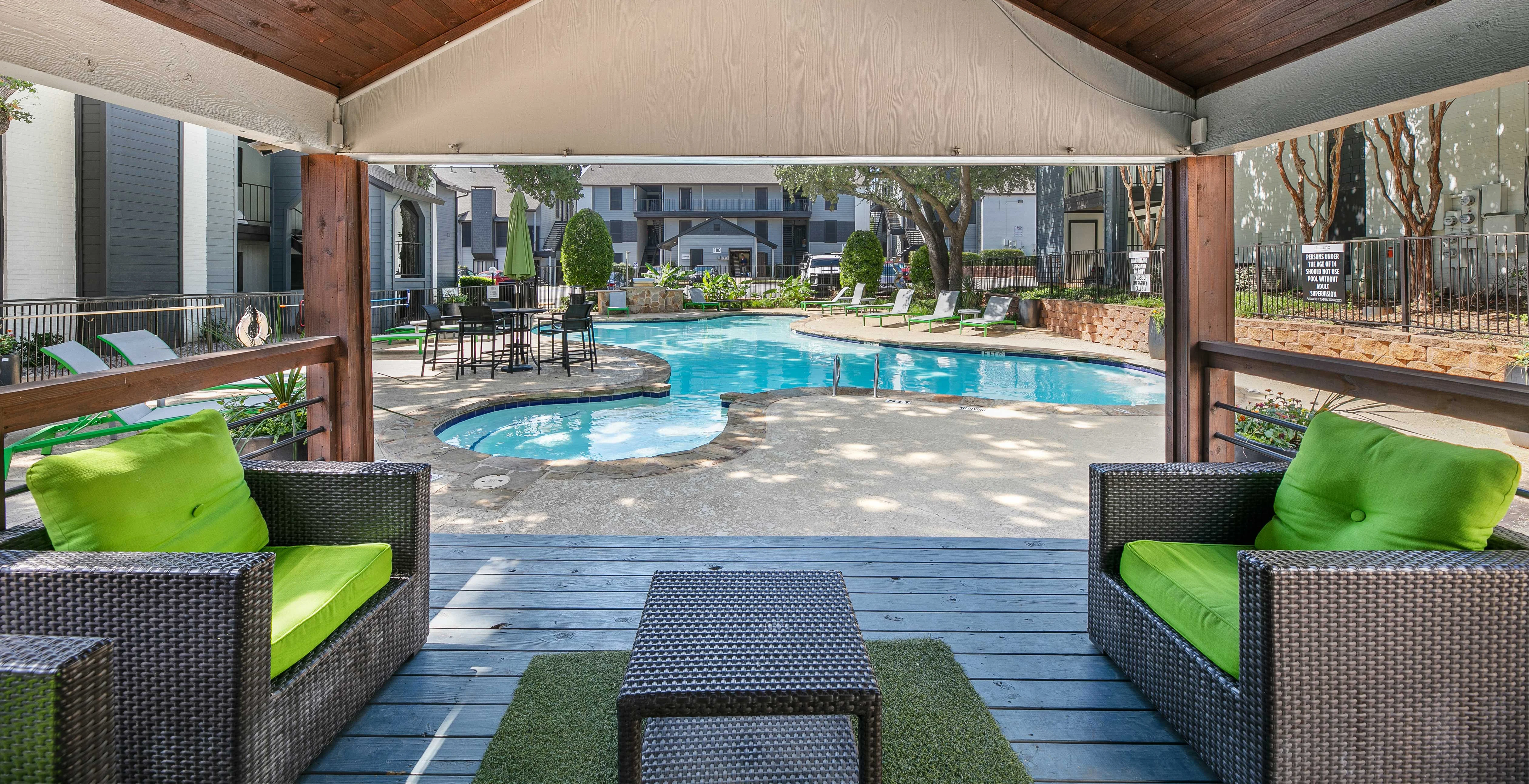 Lounge area with green chairs overlooking a swimming pool, surrounded by trees and lounge chairs.