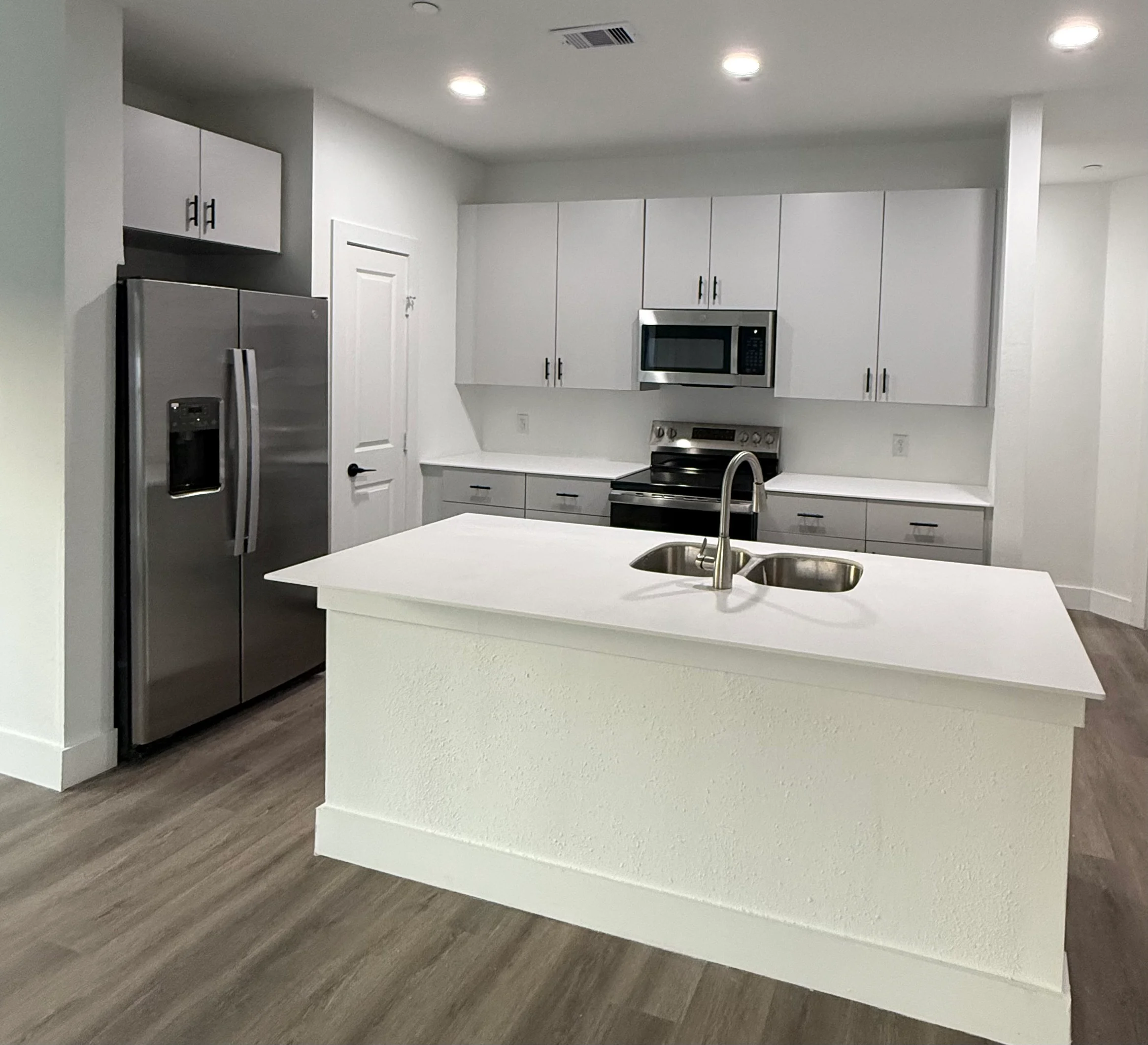 A modern kitchen featuring stainless steel appliances, a large island with a sink, white cabinets, and light hardwood flooring.